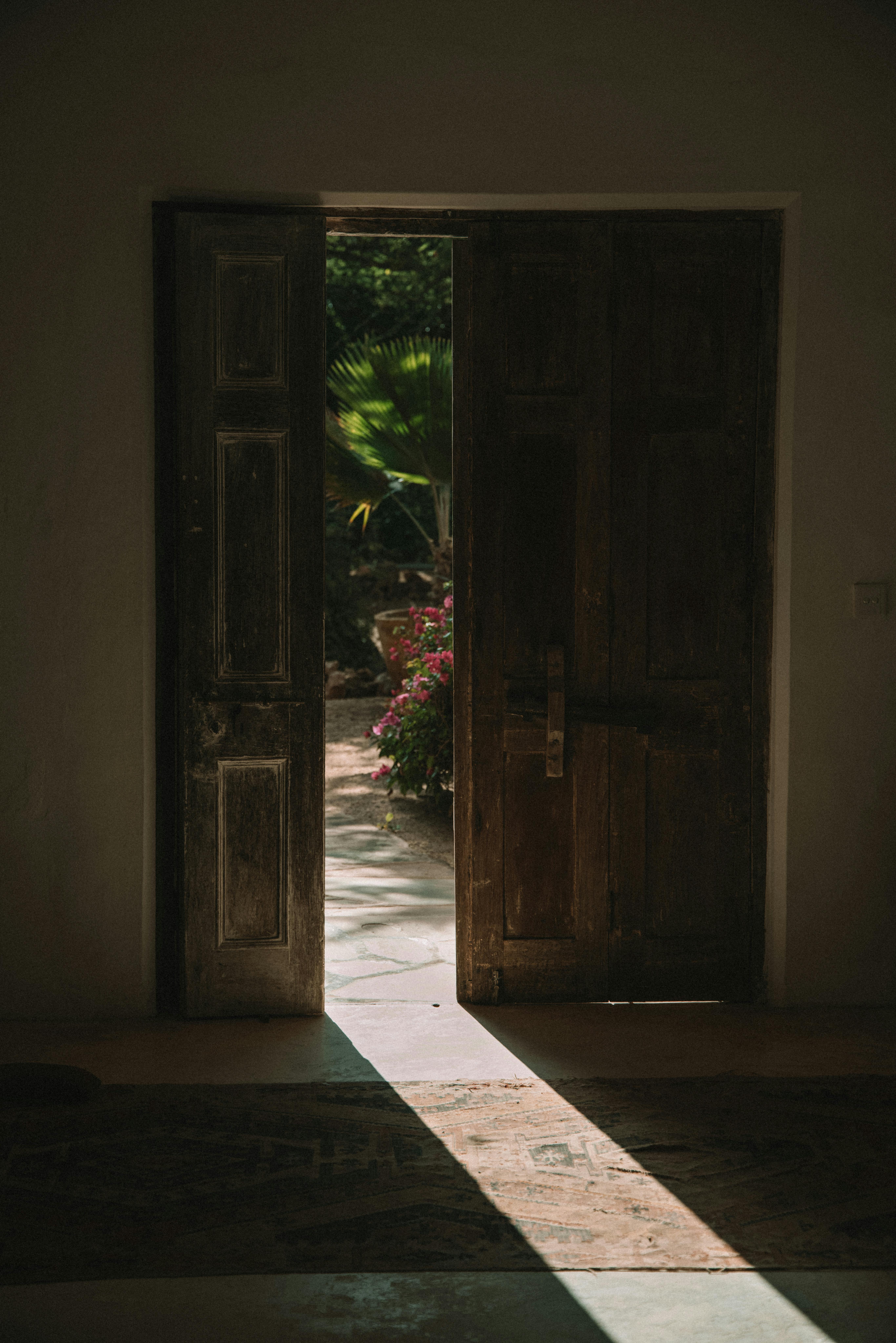 A rustic wooden door opens to reveal a sunlit garden, creating a serene and welcoming atmosphere.